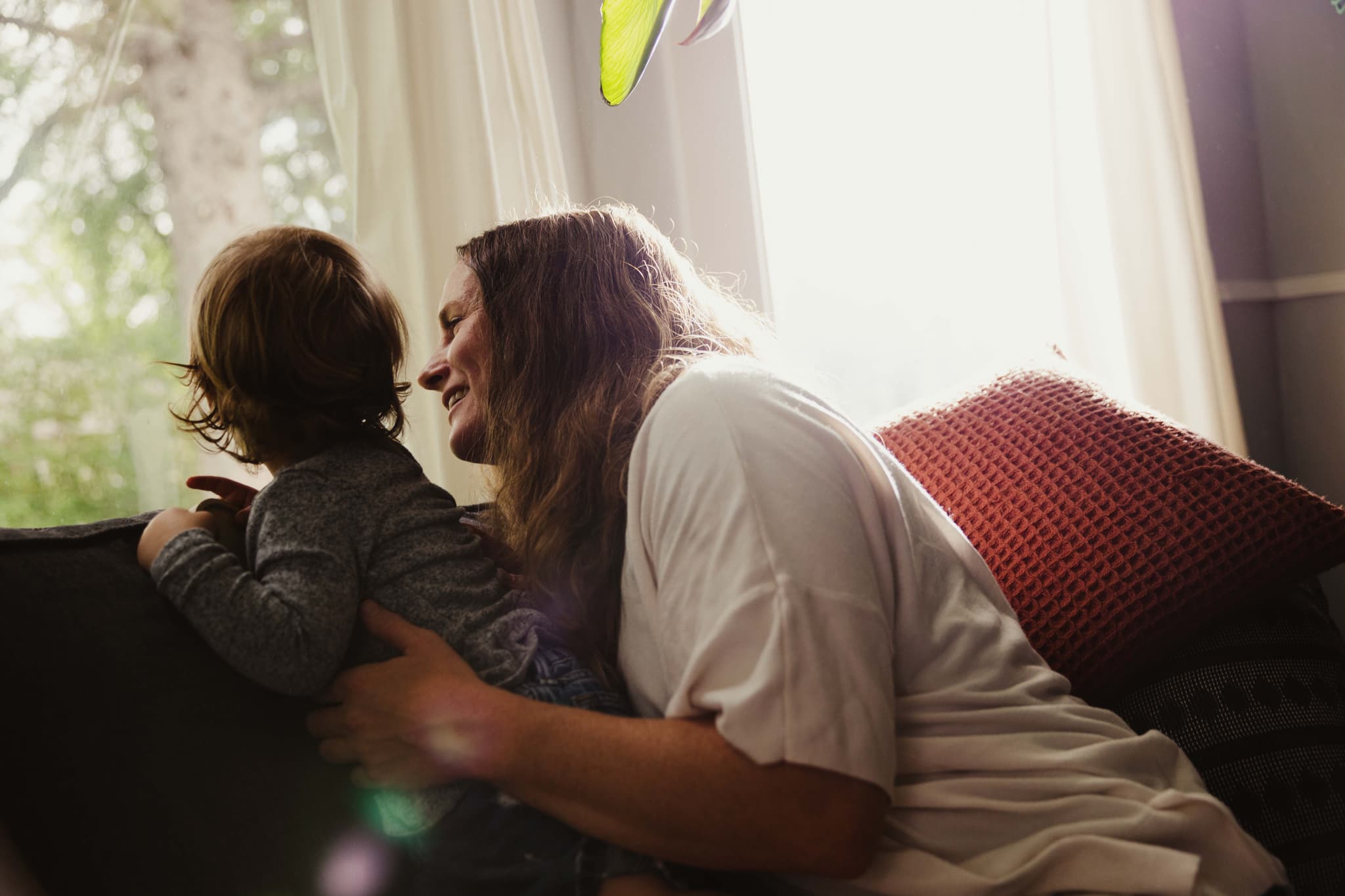 A mother and her young child sharing a quiet moment on a sofa by a bright window